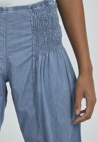 Pantalones de chambray azul claro con una cinturilla fruncida y textura recogida. Tela suave con un corte relajado y piernas ajustadas.