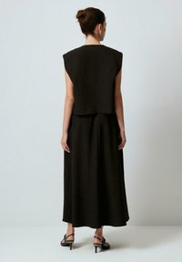 Svart, ärmlös topp med strukturerade axlar; kombinerad med en lång, svängande svart kjol. Bärs med svarta klacksandaler. Slät textur.