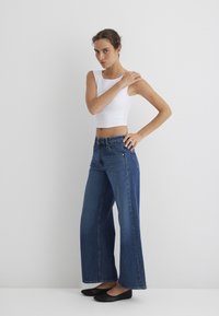 White cropped tank top paired with wide-legged blue denim jeans. The jeans have a light wash, five-pocket design, and a straight waistband.