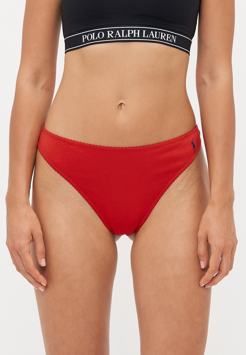 Sarkani kokvilnas bikini apakšbikses ar viļņotu malu un mazu zilu logotipu sānos. Apvienotas ar melnu ribotu sporta krūšturi.