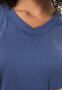 T-shirt bleu à col en V avec un col côtelé. Tissu doux et lisse avec une coupe ajustée, présentant un design épuré et simple.