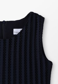 Laivastonsininen hihaton mekko, jossa on vaakasuuntaisia raitoja ja leikattuja kuvioita. Vetoketjukiinnitys ja brändilogo näkyvissä kaula-aukossa. Pehmeä rakenne.