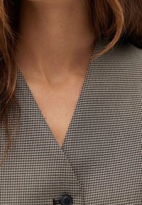 Tela de patrón pata de gallo en blanco y negro con diseño en V, que presenta un solo botón negro y una textura suave.