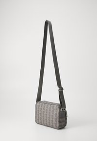 Borsa a tracolla rettangolare grigia con motivo geometrico, tracolla regolabile e chiusura con zip. Texture liscia con una finitura durevole.