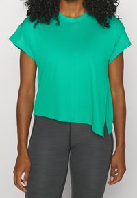 Grön kortärmad tränings-T-shirt med lös passform, texturerad tyg, sidoflikar och rundad halsringning, matchad med grå leggings.