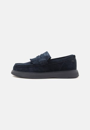 Tumesinine seemisnahast loafer tuttidega peal ja paks must kummist tald, näht külje pealt valgel taustal.