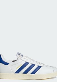 Bijela kožna tenisica s tri plave pruge, žutim natpisom "GAZELLE", zaobljenim vrhom, teksturiranom gumenom potplatom i podstavljenim plavim okovratnikom.