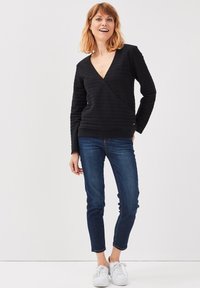 Haut noir texturé à manches longues avec un décolleté en V profond, associé à un jean skinny bleu foncé et des baskets blanches. Design simple et moderne.