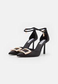 Scarpe con tacco alto in satin nero, con punta affusolata, cinturini alla caviglia e una fibbia geometrica dorata decorata con gemme trasparenti.