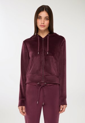 Felpa con zip color bordeaux realizzata in materiale morbido, dotata di tasca frontale, cappuccio con cordini e maniche lunghe con polsini.