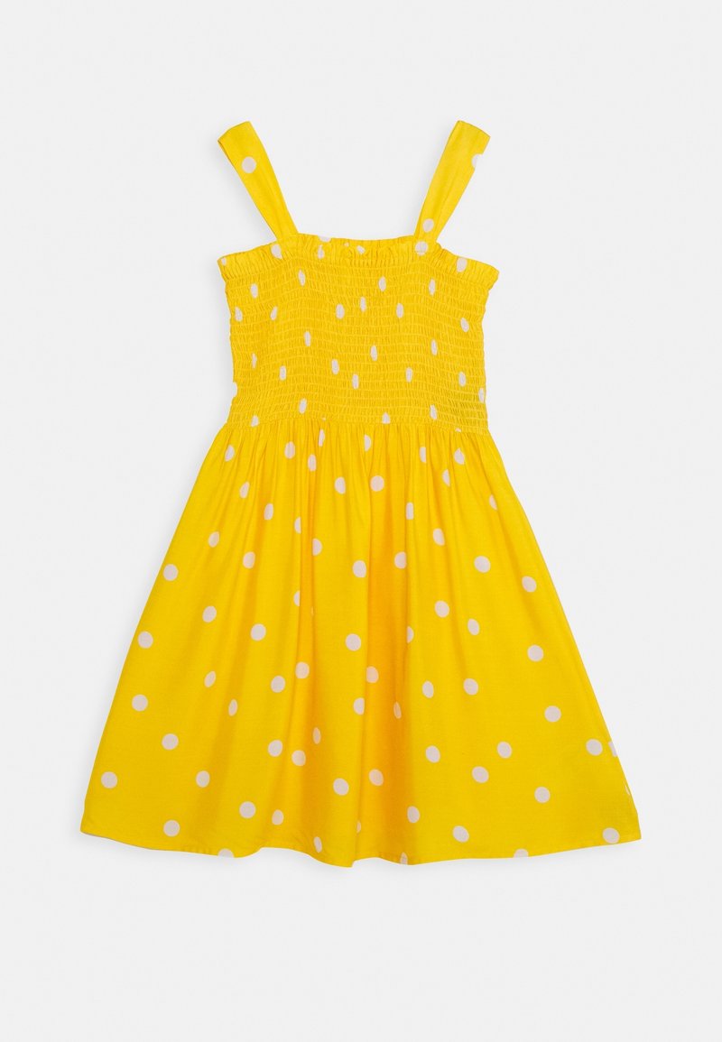 Robe jaune sans manches à pois blancs, corsage smocké et bretelles, étalée à plat sur fond blanc.