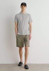 Γκρι πόλο μπλούζα, καφέ σορτς με σχέδια, μαύρο καπέλο και μαύρα παπούτσια χωρίς κορδόνια. Απλός, casual σχεδιασμός κατάλληλος για ζεστό καιρό.