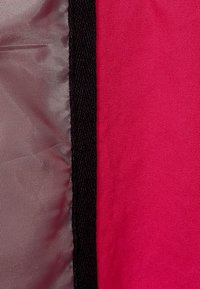 Textil med kontrasterande sektioner: starkt rosa tyg, glansigt silvermaterial och en svart kant, som framhäver olika texturer och färger.