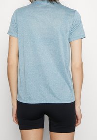 Jasnoniebieska, sportowa koszulka z krótkim rękawem o teksturowanym wykończeniu, zestawiona z czarnymi, dopasowanymi szortami. Brak widocznych logo lub wzorów.