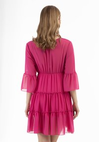 Rochie din chiffon roz cu mâneci clopot până la trei sferturi, talie plisată și design cu volane în trepte. Materialul transparent adaugă ușurință.