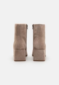 Stivali alla caviglia in suede marrone con tacco quadrato e cerniere laterali. Texture liscia e design semplice, caratterizzati da una silhouette essenziale.