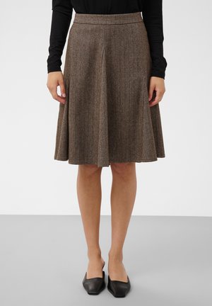 Jupe marron coupée en A longueur genou avec un motif chevron subtil, portée avec un haut noir à manches longues et des chaussures noires à bout carré.