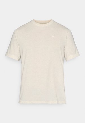 Jasnobeżowa, krótkoszlfekowa koszulka z miękkiego, teksturowanego materiału. Posiada małe, białe logo Nike na lewej stronie klatki piersiowej.