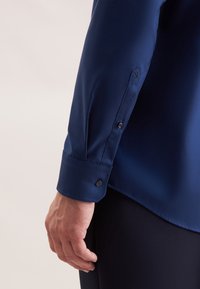 Donkerblauw overhemd met lange mouwen van gladde stof, met knoopmanchetten en een slank ontwerp, gecombineerd met donkere broeken.