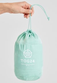 Light mint green drawstring bag with mesh accents and white logo, cylindrical shape, made of soft material, held by a hand.