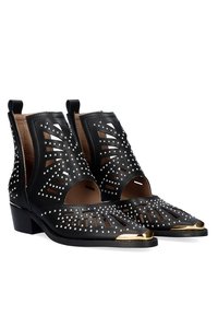 Botines de cuero negro con diseño recortado, tachuelas plateadas y punta dorada. Tacón bajo, lados abiertos y acabado texturizado.