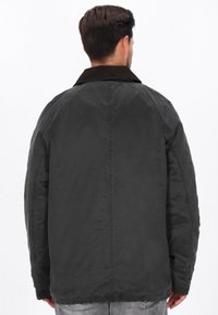 Zwarte jas met een corduroy kraag, gemaakt van een gladde, gestructureerde stof, raglanmouwen en een rechte snit, gezien van de achterkant.