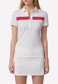 Biała koszulka polo z krótkim rękawem, z poziomą czerwoną paską na klatce piersiowej i dopasowanym krojem, zestawiona z pasującą spódnicą.