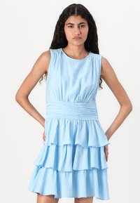 Απαλό μπλε, αμάνικο φόρεμα από μαλακό ύφασμα. Ο ραμμένος κορσές και η κλιμακωτή φούστα με βολάν προσθέτουν υφή και διάσταση. Απλή στρογγυλή λαιμόκοψη.