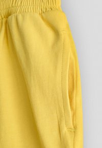 Primo piano della fascia elastica gialla in vita e della tasca laterale su pantaloni in tessuto morbido.