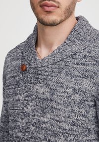 Strikket sweater med tekstur i marineblå og grå, med en bred sjalskrave og en brun knapdetalje på siden.