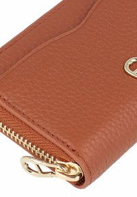 Braune Lederbrieftasche mit Goldreißverschluss und Verschluss. Auf der Außenseite befindet sich ein dezentes Wellenmuster für zusätzliche Details.