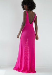 Sukienka z dekoltem w serek, bez pleców, w intensywnym różowym kolorze, z dzianiny o luźnym kroju. Pełna długość, z teksturowanym wzorem i swobodną sylwetką.