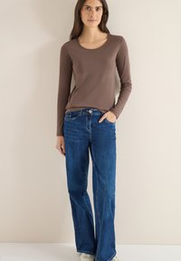 Hnědá košile s dlouhým rukávem ve spojení s modrými širokými džínami. Hladká látka, výstřih do oblouku a klasický denimový design s světlejšími okraji u lemu.