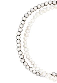 Dvě náhrdelníky: jeden s kulatými stříbrnými korálky a druhý s nepravidelnými bílými perlami, které vykazují různé textury a tvary.