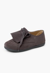 Zapato de ante gris con puntera redondeada, flecos decorativos y cierre de cordones. Suela de goma negra, revestimiento interior suave y diseño de perfil bajo.