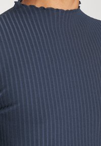 Haut en maille côtelée marine avec col montant et bordure festonnée. Présente des rayures verticales, une texture douce et une silhouette ajustée.