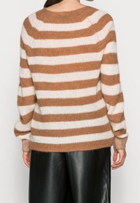 Gestreifter Pullover mit horizontalen hellbraunen und cremefarbenen Streifen, rundem Ausschnitt, gerippten Bündchen und lockerem Schnitt. Kombiniert mit schwarzen Lederhosen.