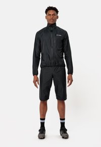 Giacca leggera nera con tasca con zip, polsini elasticizzati e pantaloni corti abbinati. Texture liscia, design compatto, adatta per attività all'aperto.