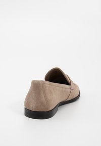 Chaussure beige en daim à enfiler avec un petit talon noir, vue de l'arrière sur fond blanc.