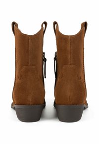 Stivaletti in suede marrone con tacco basso, linee superiori curve, linguette di estrazione e cerniere laterali per una facile calzata. Suola in gomma liscia e resistente.