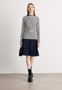 Schwarz-weiß gestreiftes Langarmoberteil, kombiniert mit einem marineblauen Rock. Das Outfit zeichnet sich durch eine lockere Passform, eine gepflegte Textur aus und wird durch schwarze Fußbekleidung ergänzt.