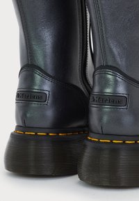 Primer plano de botas Dr. Martens de cuero negro que muestran las pestañas traseras con el logo y el característico costura amarilla en las suelas.
