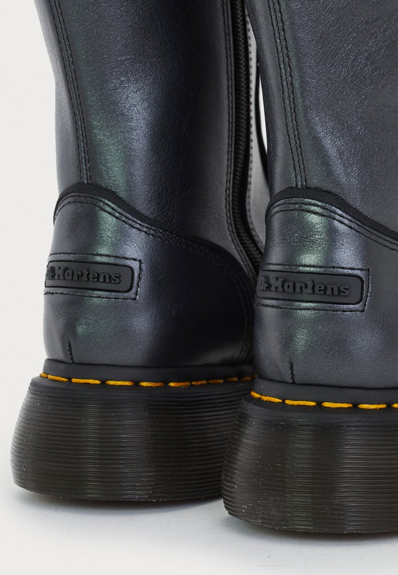 Nærbillede af sorte læder Dr. Martens støvler, der viser bagsidehæl-lapper med logo og signaturgul syning på sålerne.