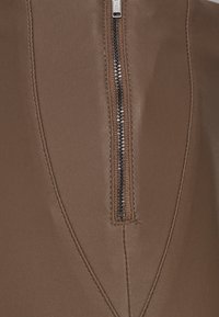 Vêtement en simili cuir marron avec une fermeture éclair visible, mis en valeur par de fins surpiqures le long des bords et une finition lisse et texturée.