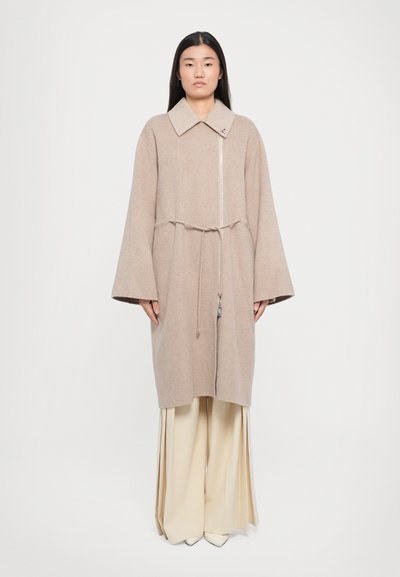Beige Wollmischungsmantel mit großem Kragen, vorderem Reißverschluss, tailliertem Schnitt und breiten Ärmeln. Getragen über cremefarbenen, weiten Hosen.