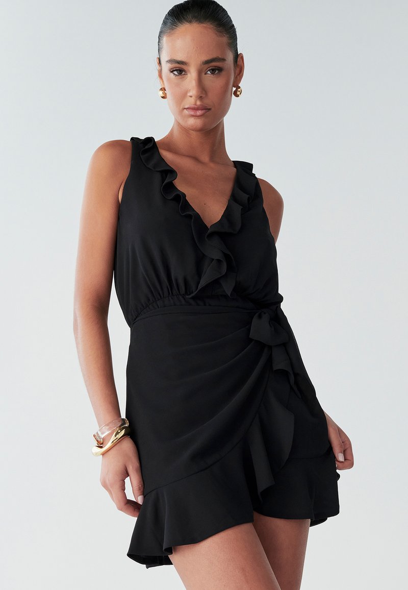 Schwarzes Kleid mit gerüschtem V-Ausschnitt, tailliertem Bund und ausgestelltem Rock mit einer Schleife als Akzent. Glatter, leichter Stoff.