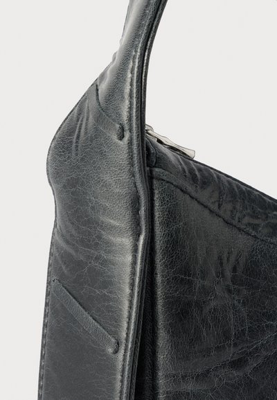 Κοντινό πλάνο μαύρης υφασμάτινης δερμάτινης τσάντας που δείχνει τη σύνδεση της λαβής και λεπτομέρειες φερμουάρ σε ουδέτερο φόντο.