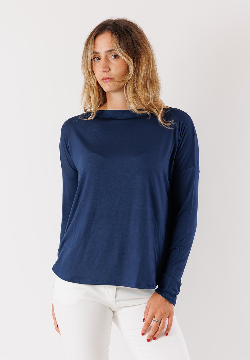Maglietta a maniche lunghe blu navy con vestibilità comoda, tessuto morbido, scollatura a girocollo e maniche allungate, abbinata a pantaloni slim-fit di colore chiaro.