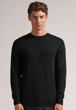 Pull en tricot noir avec un col rond, des manches longues, des poignets et un ourlet côtelés, présentant une texture lisse et un style minimaliste.