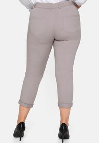 Pantalons cropped gris clair avec ourlets retroussés, dotés de deux poches arrière, texture lisse, associés à des chaussures à talons noirs.